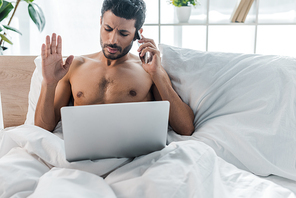 handsome bi-racial man with laptop talking on smartphone in morning