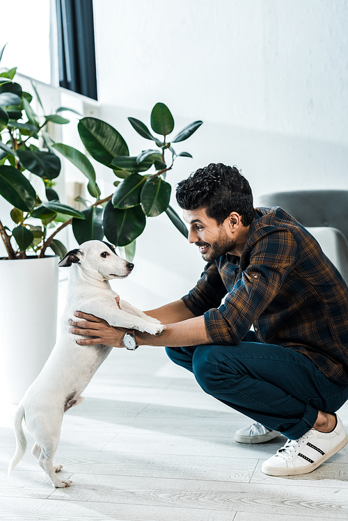 side view of handsome and smiling bi-racial man holding jack russell terrier