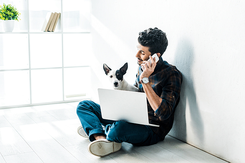 handsome bi-racial man talking on smartphone and holding jack russell terrier