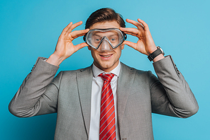 smiling businessman putting diving mask on face on blue background