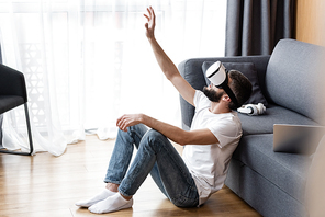 Side view of man using vr headset near laptop and headphones on couch