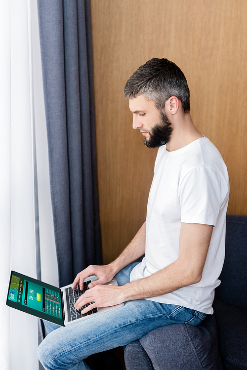 Side view of man using laptop with sports bet website on couch