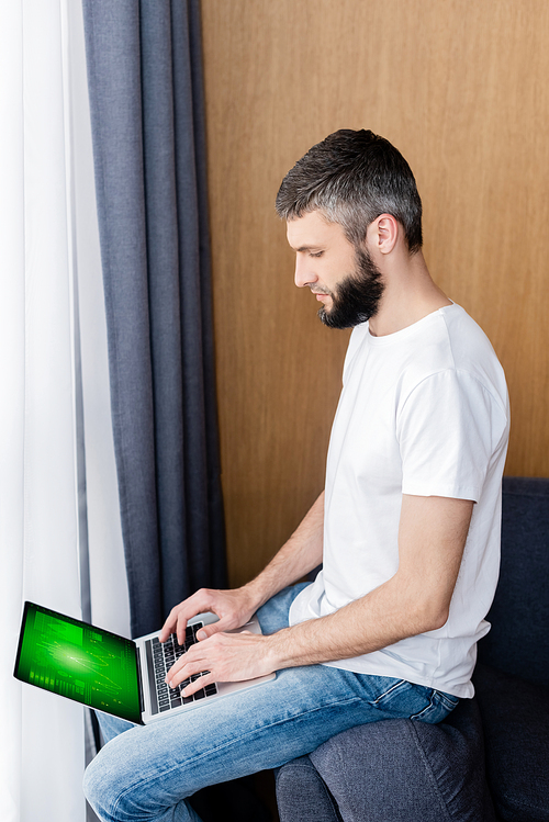 Side view of man using laptop with charts and graphs on screen in living room