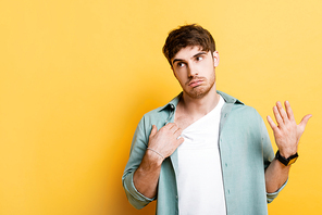 displeased young man touching shirt and waving hand while suffering from heat on yellow