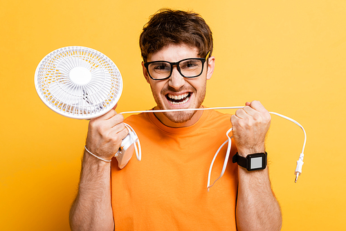 angry man in eyeglasses holding broken electric fan on yellow