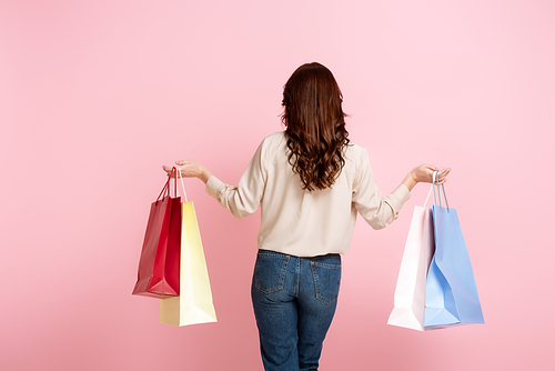 Back view of woman holding colorful shopping bags isolated on pink