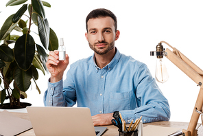handsome freelancer holding hand sanitizer near laptop isolated on white