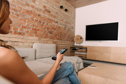 young woman holding remote controller and watching tv with blank screen during self isolation, selective focus