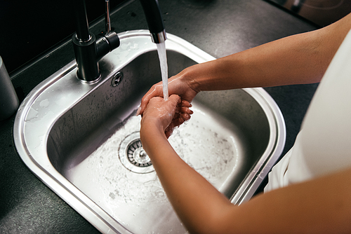 cropped view of woman washing hands in sink in kitchen during quarantine