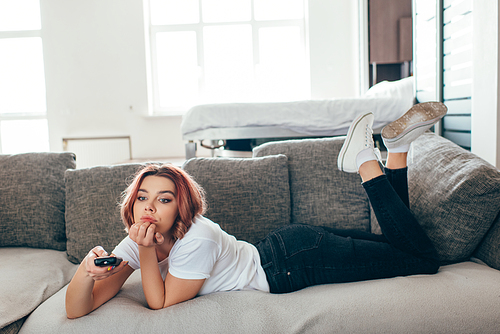 bored woman with remote controller watching tv at home on self isolation