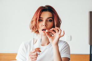 attractive girl eating pill and holding glass of water at home on self isolation