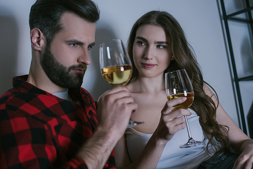 smiling girl looking at dreamy boyfriend while sitting together with glasses of white wine