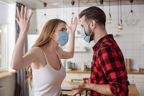 young couple in medical masks quarreling while girl screaming and gesturing with raised hands