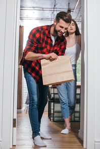 joyful man looking in paper bag with delivered food near attractive girlfriend