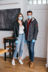 young couple in protective masks and latex gloves  while standing near door