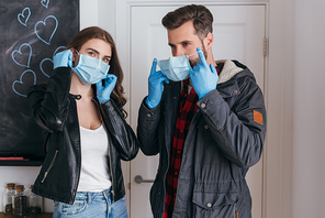 young couple in latex gloves putting on protective masks before leaving home