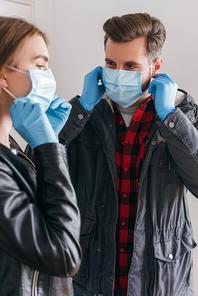 young couple in latex gloves putting on protective masks before leaving home