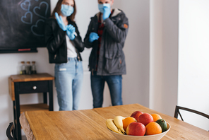 selective focus of young couple in medical masks and latex gloves, and bowl of fresh fruits on table