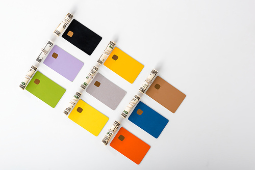 top view of multicolored credit card templates near cash rolls on white