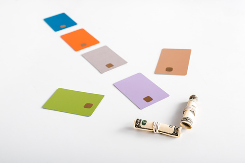 selective focus of colorful credit card templates and cash rolls on white