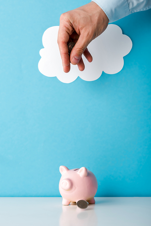 cropped view of man throwing coin near pink piggy bank on blue