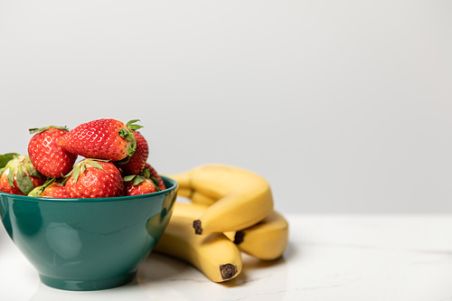 sweet and tasty strawberries in bowl near yellow bananas on grey