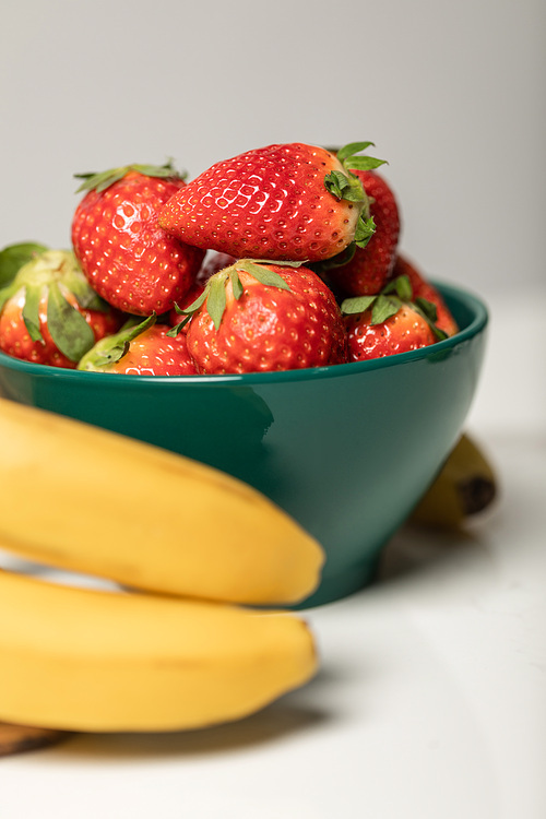 selective focus of sweet strawberries in bowl near yellow bananas on grey