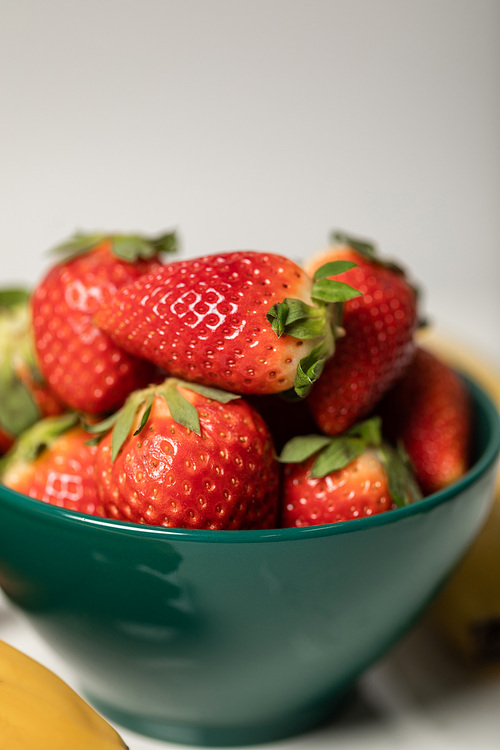 selective focus of red sweet and organic strawberries in bowl on grey