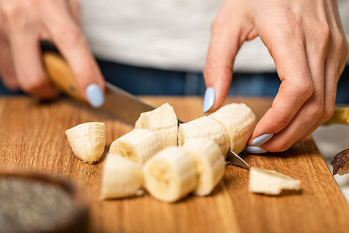 cropped view of woman cutting ripe and sweet bananas on cutting board
