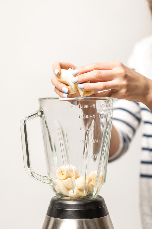 cropped view of woman putting ripe sweet bananas in blender on white