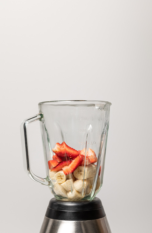 sweet strawberries and slices of ripe bananas in blender on grey