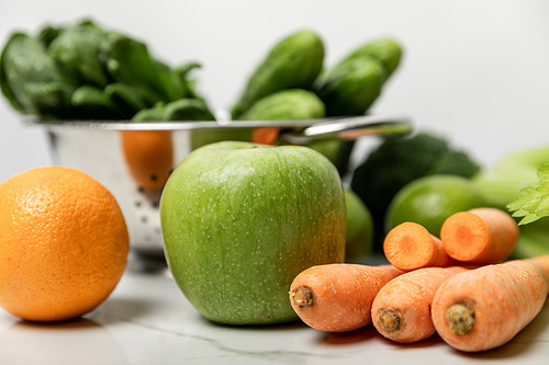 selective focus of green apple, orange and carrots near green cucumbers on white