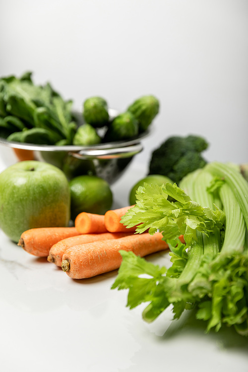 selective focus of celery near carrots, ripe apple and green vegetables on grey