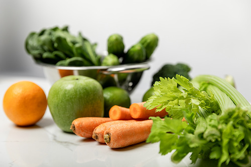 selective focus of celery near sweet carrots, ripe apple and green vegetables on grey