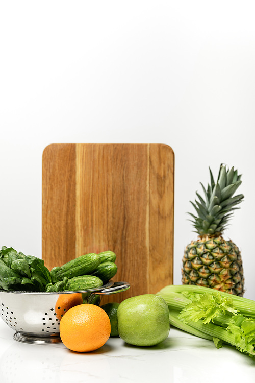 ripe fruits near fresh vegetables and wooden cutting board on white