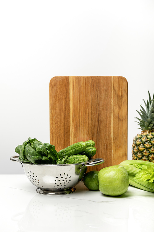 ripe fruits near fresh green vegetables and wooden cutting board on white
