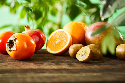 selective focus of kiwi, oranges, pomegranate, mango and persimmons on wooden table
