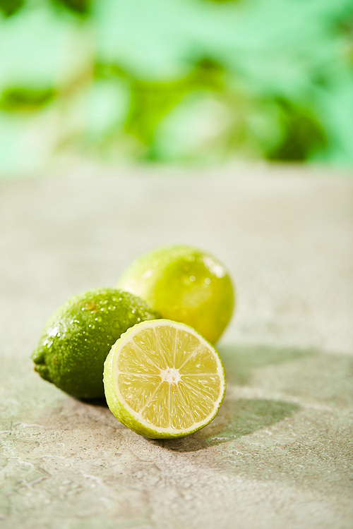 selective focus of whole and cut limes with drops on marble surface