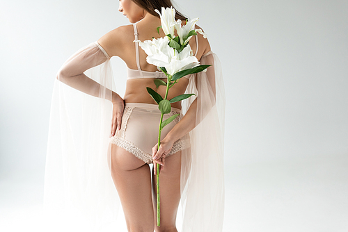 back view of delicate young woman in beige lingerie and mesh sleeves holding bouquet of lilies isolated on white
