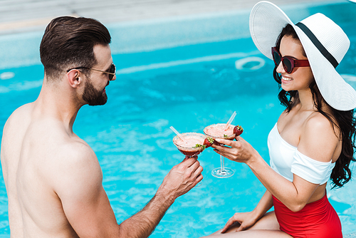 happy man clinking cocktail glasses with woman in straw hat