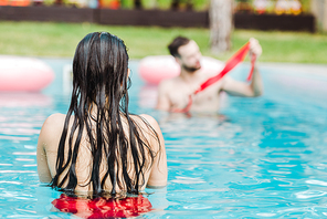 back view of woman swimming in swimming pool near man