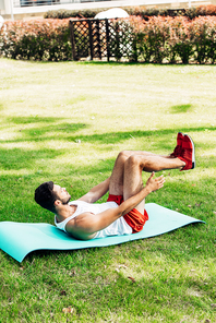 handsome man in sportswear doing do abs on fitness mat outside