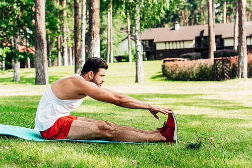 profile of handsome sportsman doing stretching exercise on fitness mat