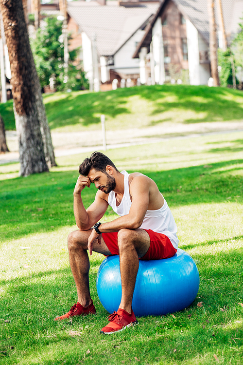 upset sportsman sitting on blue fitness ball in park