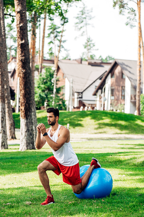 handsome bearded sportsman working out on fitness ball in park