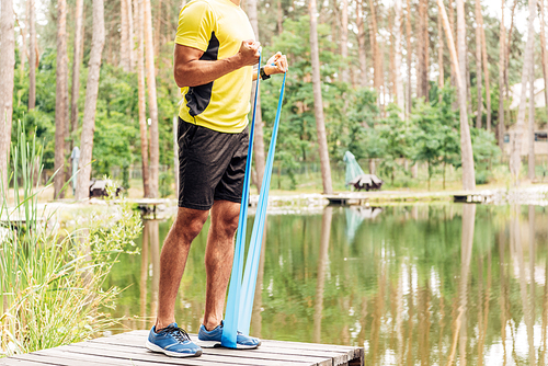 cropped view of sportsman exercising with suspension straps near lake