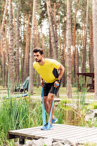 handsome man exercising with suspension straps near lake in forest