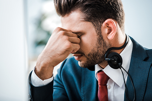 tired businessman in headset with closed eyes covering face in office