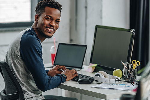 cheerful african american programmer  while sitting near computers