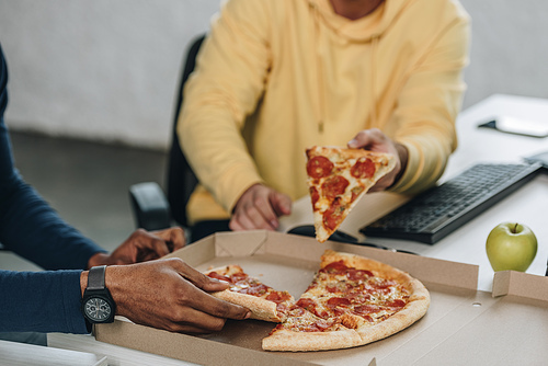 cropped view of two multicultural programmers eating pizza in office